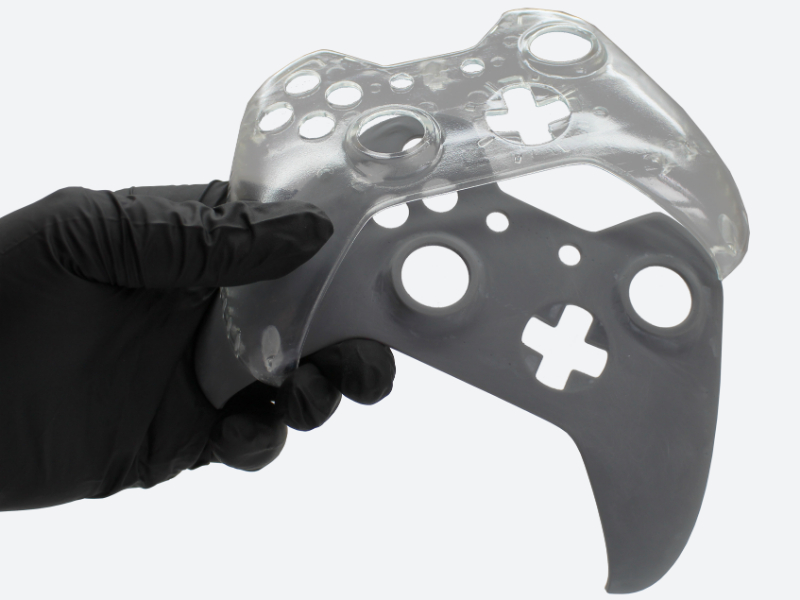 Gloved hand holding a video game controller faceplate 3D printed in clear and grey plastic