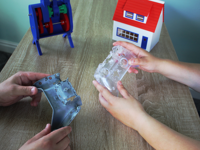 Two people holding 3D printed parts over a table with parts in the background